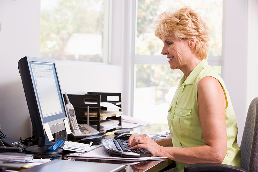 Older woman working at a computer on her desk.