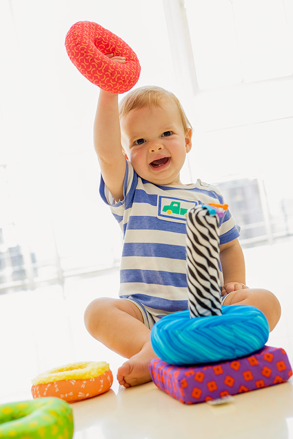 Baby playing with soft rings and trying to stack them on a tower.