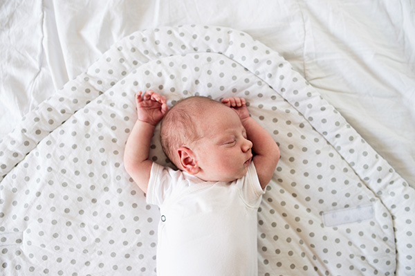 Newborn sleeping alone in a crib on his back.