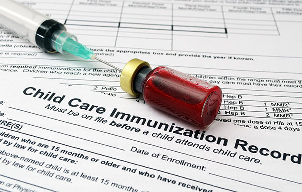 Hypodermic needle in vial laying on Child Care Immunization Record.